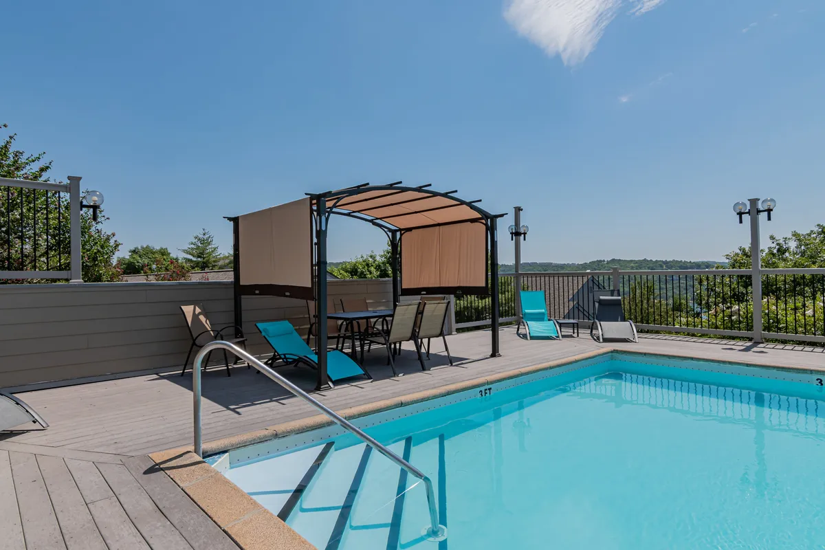 A vibrant outdoor swimming pool is surrounded by a landscaped area with deck chairs and a covered seating space. The pool is easily accessible, inviting guests to relax, swim, or socialize in a leisurely resort setting, and is ideal for families or anyone seeking lakeside leisure.