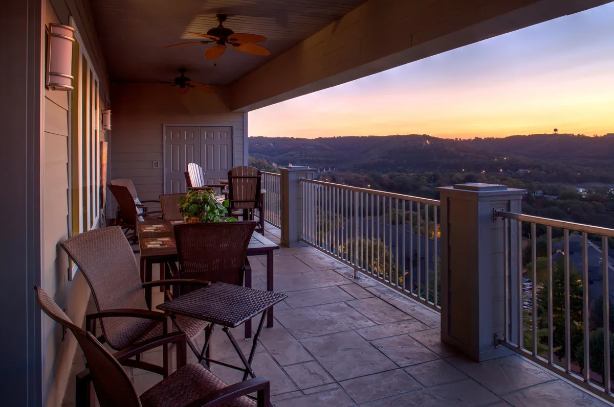 An extra-large deck furnished with comfortable chairs and a table overlooks a sweeping landscape at sunset. The view extends toward the lake, with gentle hills in the background, creating an inviting spot for group gatherings or quiet moments. The tranquil lighting and spacious outdoor setting are perfect for shared meals or sunset conversations.