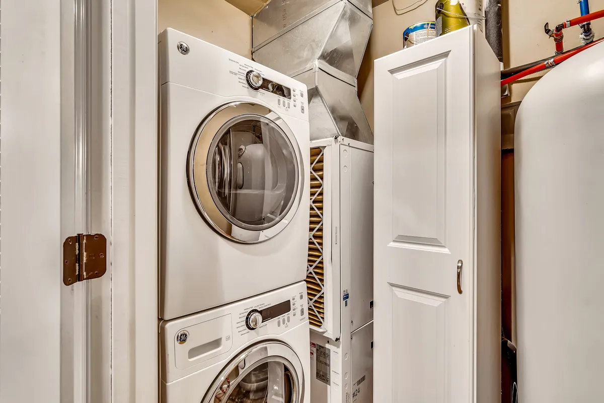This image shows a dedicated laundry room with a stacked washer and dryer, a white storage cabinet, and a ventilation duct. The space is organized and practical, highlighting the in-unit laundry convenience for longer stays.