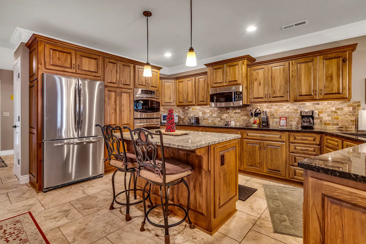 This image highlights a spacious kitchen featuring a stainless steel refrigerator, granite countertops, warm wood cabinetry, and inviting bar stools. The setting captures the essence of a modern, fully equipped kitchen designed for both everyday cooking and festive gatherings.