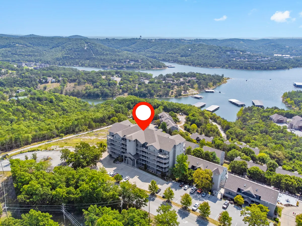 A wide exterior view of the main resort building amidst lush greenery, overlooking a tranquil lake with mountains in the background. The setting sun adds a warm, inviting glow, and there are hints of outdoor activity areas near the shoreline.