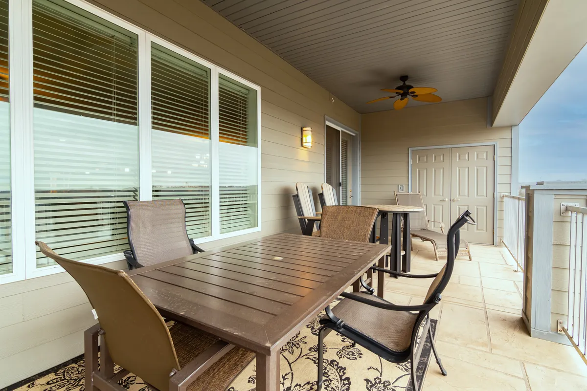An extra-large private deck furnished with a comfortable outdoor dining table and chairs. The deck features a decorative rug, ceiling fan for comfort, and sliding glass doors that visually connect the interior living and dining areas to the outdoors. The view from the deck is inviting, offering a place for group breakfasts, sunset dinners, or festive gatherings in the fresh air.