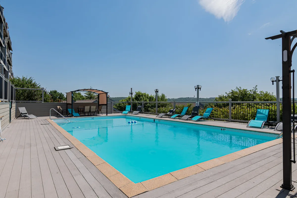 A sparkling outdoor swimming pool surrounded by lounge chairs, a cabana, and lush landscaping. The scene is bright and cheerful, inviting relaxation and social gatherings during the resort's summer season.