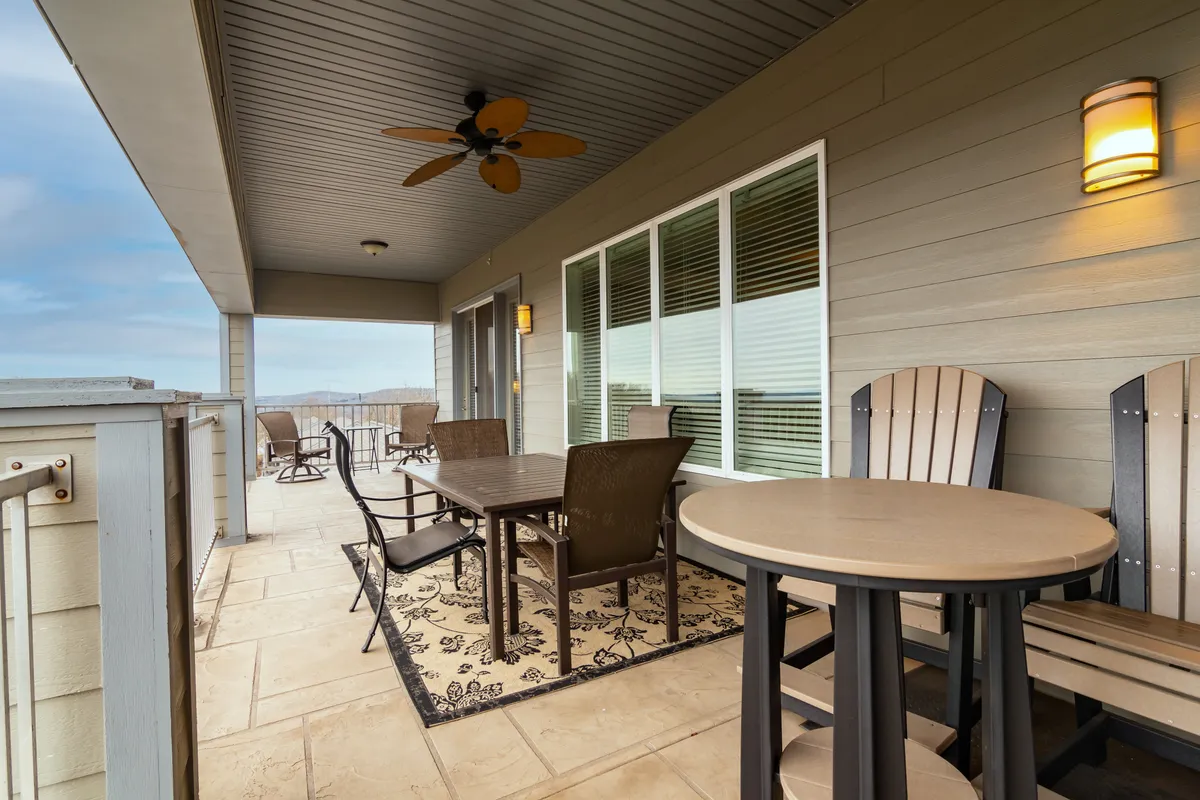 A cozy outdoor dining area featuring a table, chairs, and a ceiling fan, set on a covered patio with large windows overlooking the landscape. The setup invites guests to enjoy alfresco meals, sunset drinks, and quality time outdoors in comfort.
