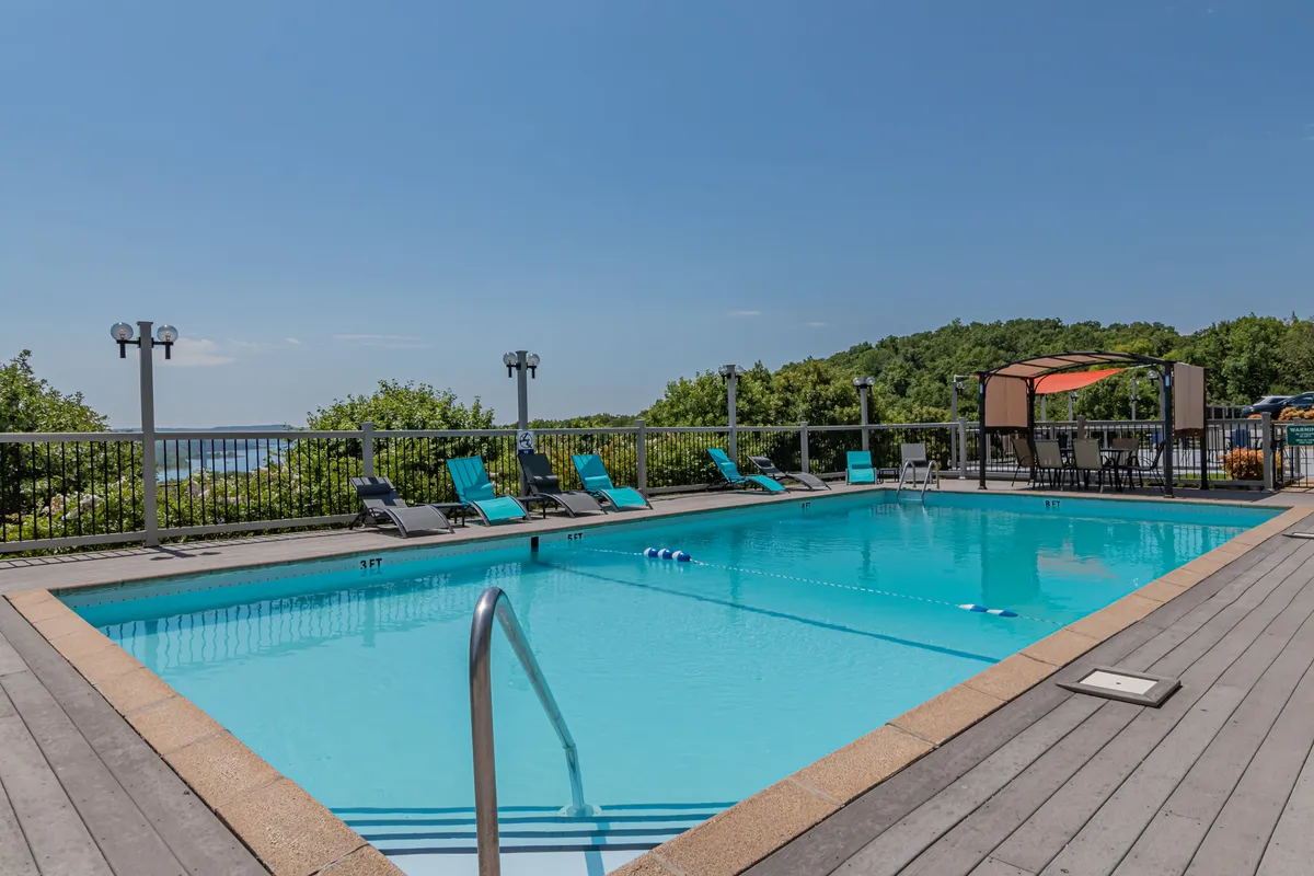A sparkling outdoor swimming pool with lounge chairs and a cabana, surrounded by manicured greenery. The inviting pool area is set against a backdrop of resort buildings, signaling a relaxing and fun community atmosphere.
