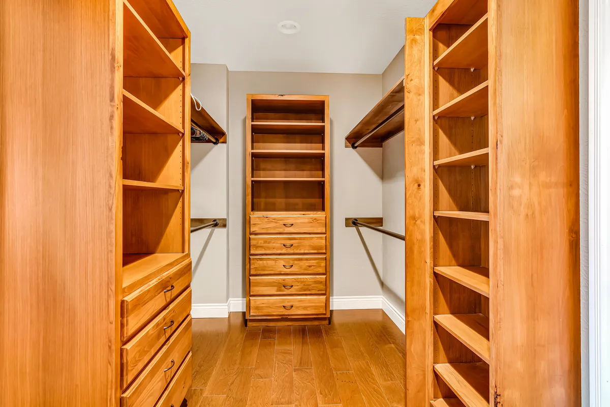 A walk-in closet with neatly arranged wooden shelving units and a central drawer unit, providing ample storage and an organized, spacious feel.