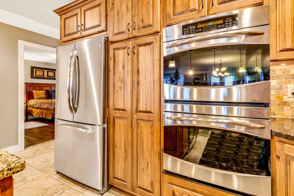 This image presents a modern kitchen with a prominent stainless steel refrigerator, gleaming double ovens, granite countertop, and elegant wood cabinetry. The overall mood is warm and welcoming, ideal for group culinary activities.