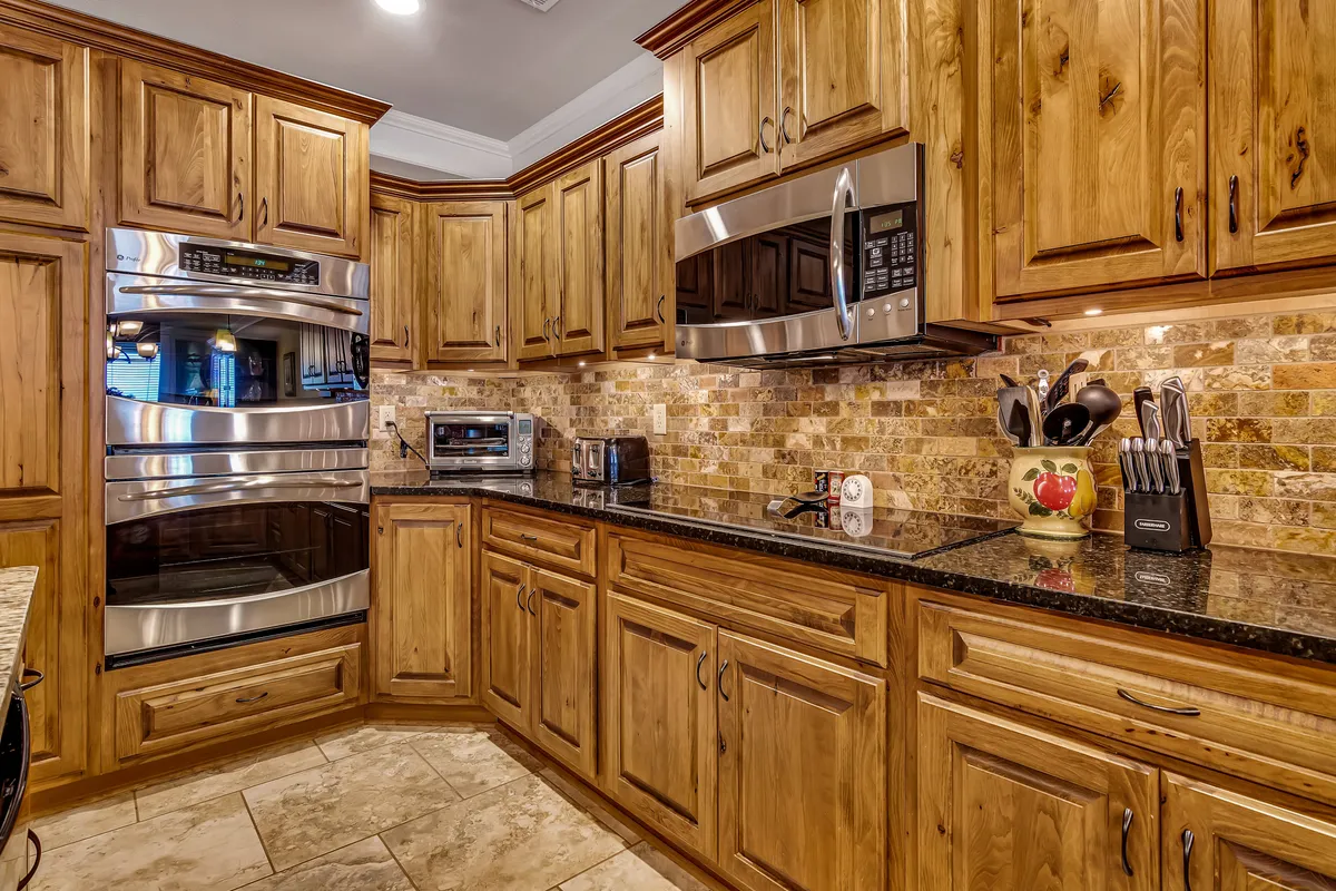 The kitchen is shown with stainless steel appliances, granite countertops, warm wooden cabinets, and colorful utensils. The setup exudes a cozy, lived-in feel perfect for hosting gatherings, baking, and meal prep.